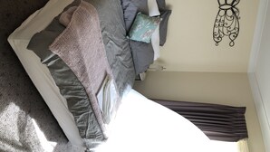A neatly made bed with multiple pillows and a blanket, a wall-mounted decorative piece, and a window with curtains.