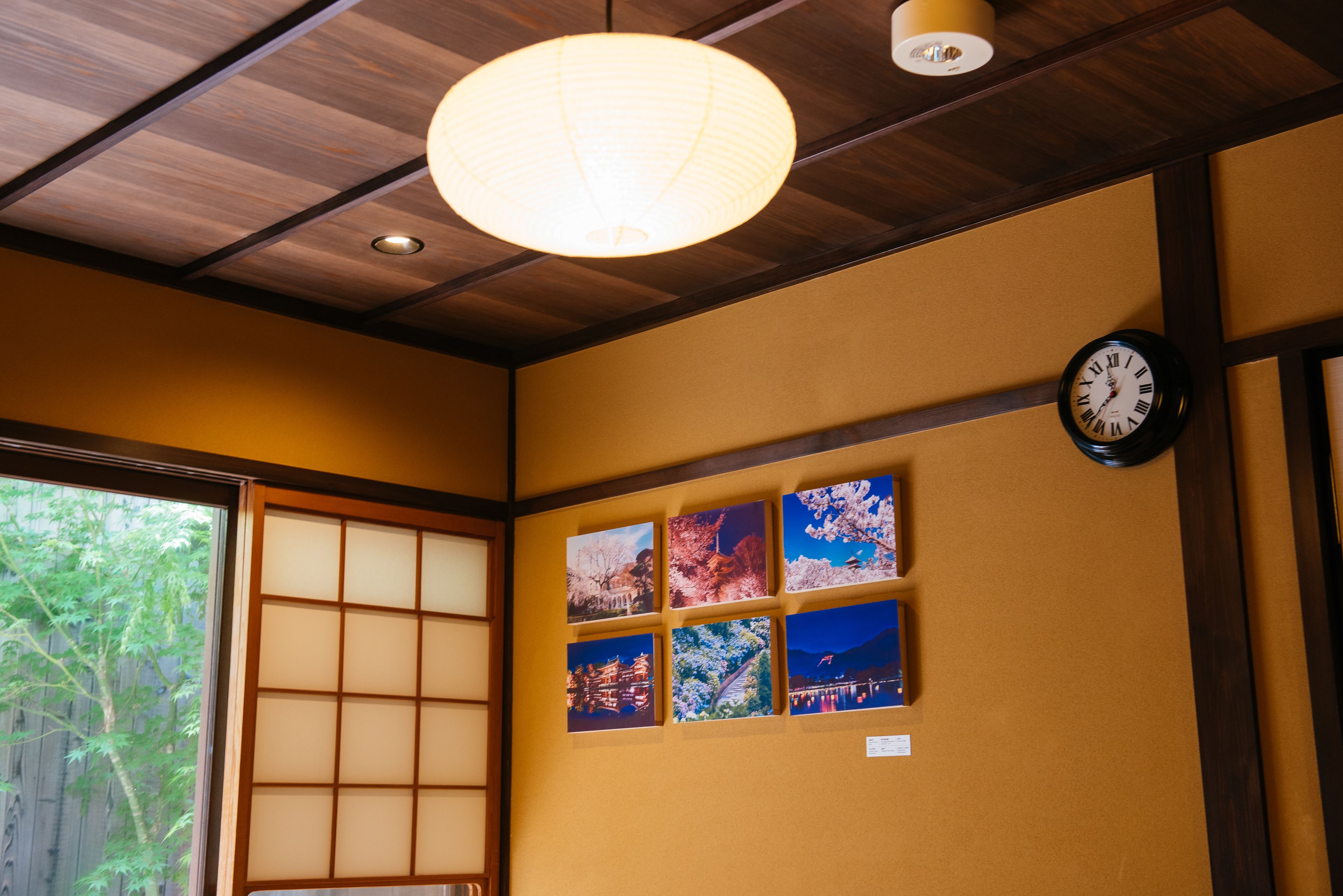 A room with a wooden ceiling, a traditional Japanese shoji screen, a wall clock, and four framed pictures.