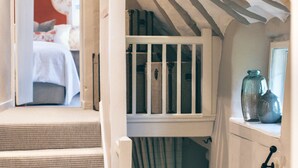 Un escalier avec une rampe blanche, une fenêtre avec des rideaux et une étagère ornée de pots décoratifs.