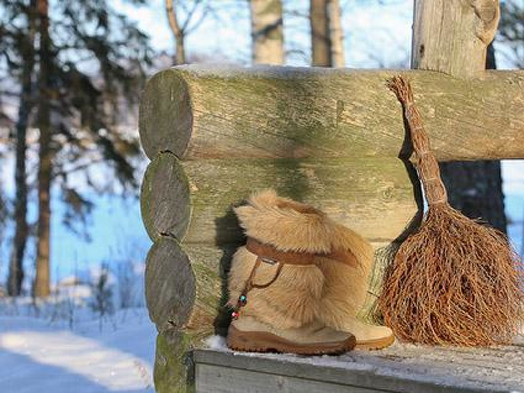 A wooden bench with a pair of boots and a broom leaning against it.