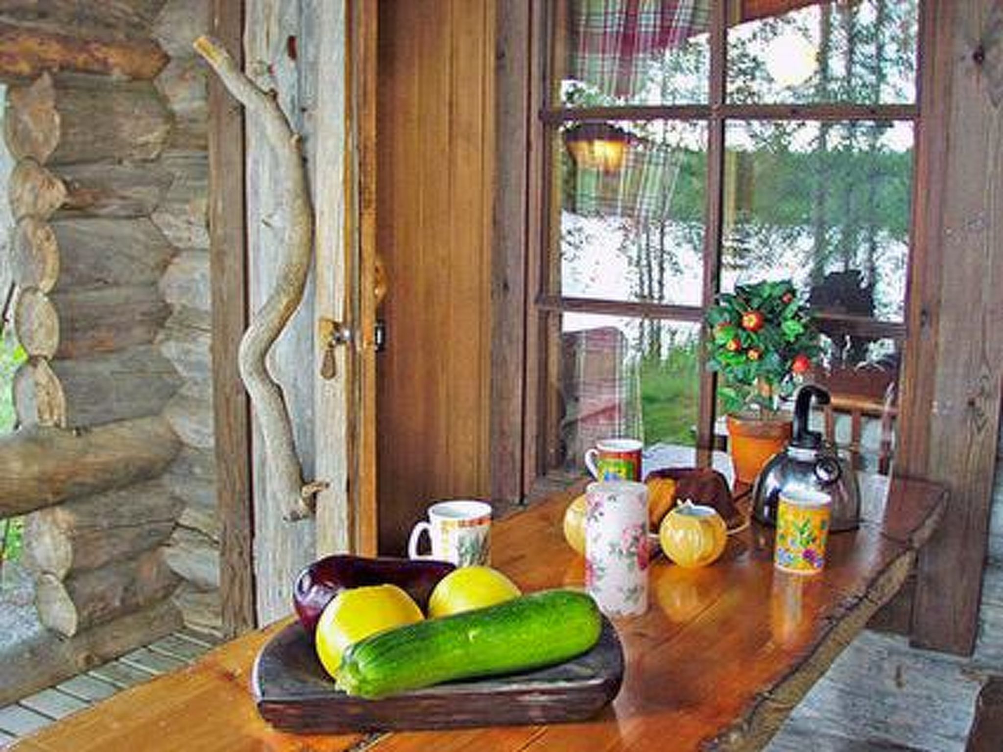 A rustic wooden table with a fruit bowl containing lemons and a cucumber, a teapot, and a mug.