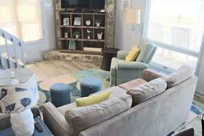 Sala de estar com sofá, banquinho e televisão em uma parede de pedra.