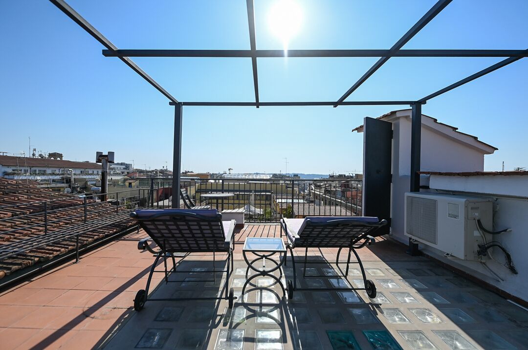 Terraza en la azotea con dos tumbonas y una mesa, con vistas a un paisaje urbano.
