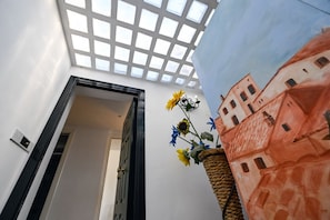 Quarto com claraboia, porta que dá para outro cômodo e parede com um mural arquitetônico pintado.