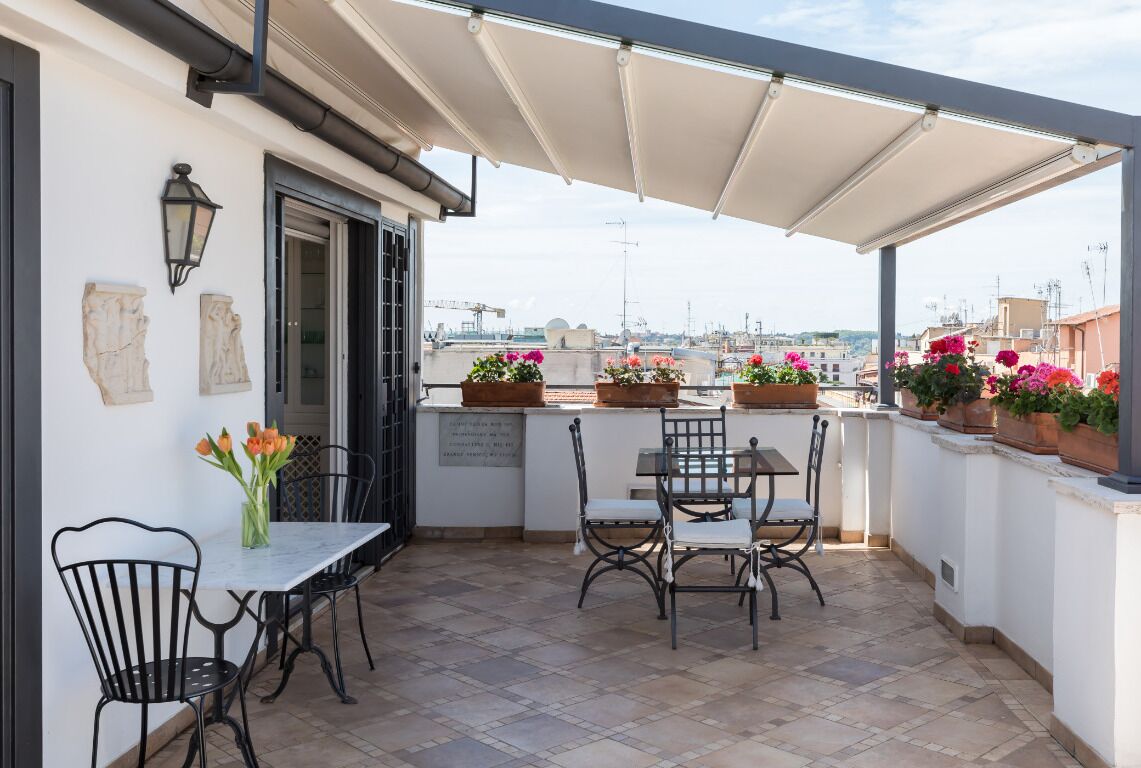 A terrace with a table and chairs, a potted plant, and a view of the cityscape.