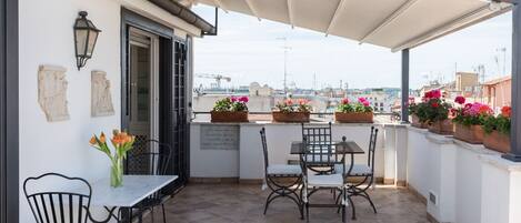 A terrace with a table and chairs, a potted plant, and a view of the cityscape.