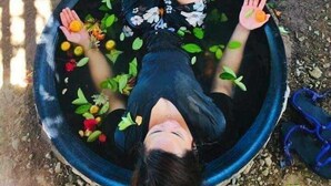 Una persona recostada sobre una cuenca circular llena de agua y flores flotantes.