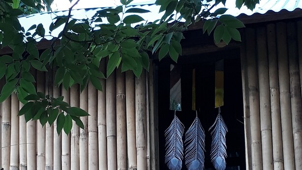 Estructura de bambú con una ventana que muestra adornos de plumas.