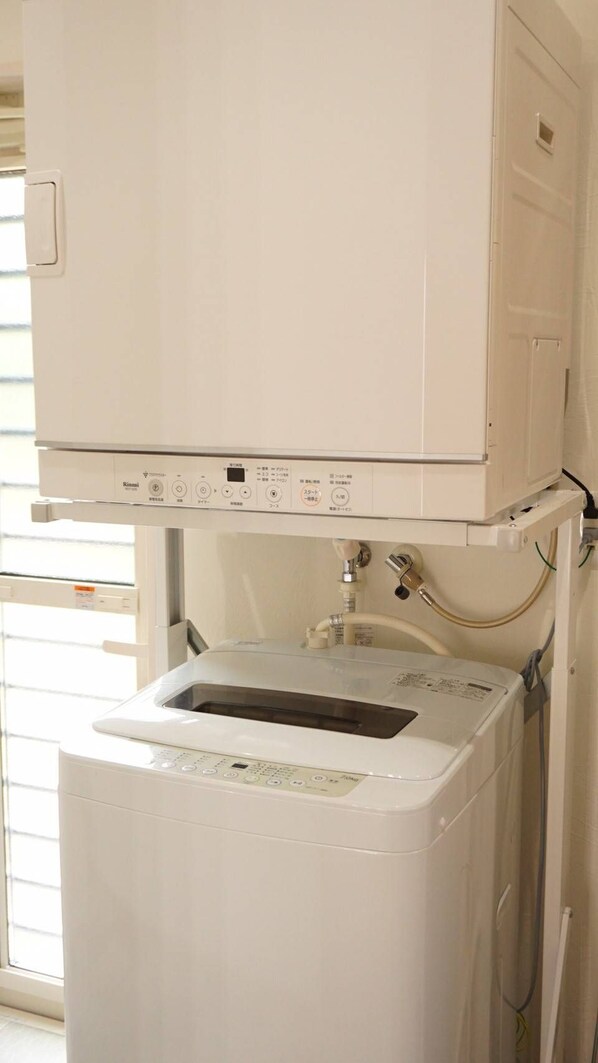 A white washing machine with a control panel, connected to a water inlet and outlet. - guest house Holoholo beach side - Hostel (Ishigaki)