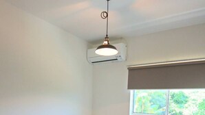 Un dormitorio con cama, ventana, una mesita y un equipo de aire acondicionado.