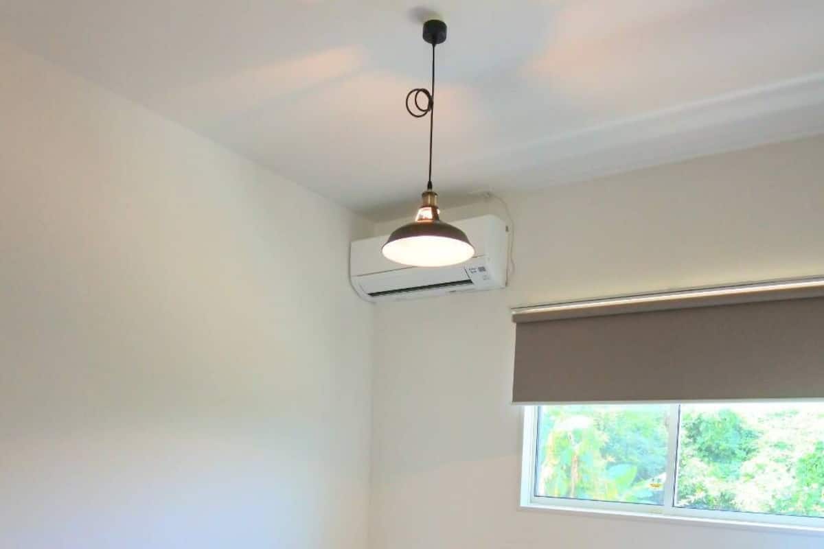 A bedroom with a bed, a window, a small table, and an air conditioning unit.
