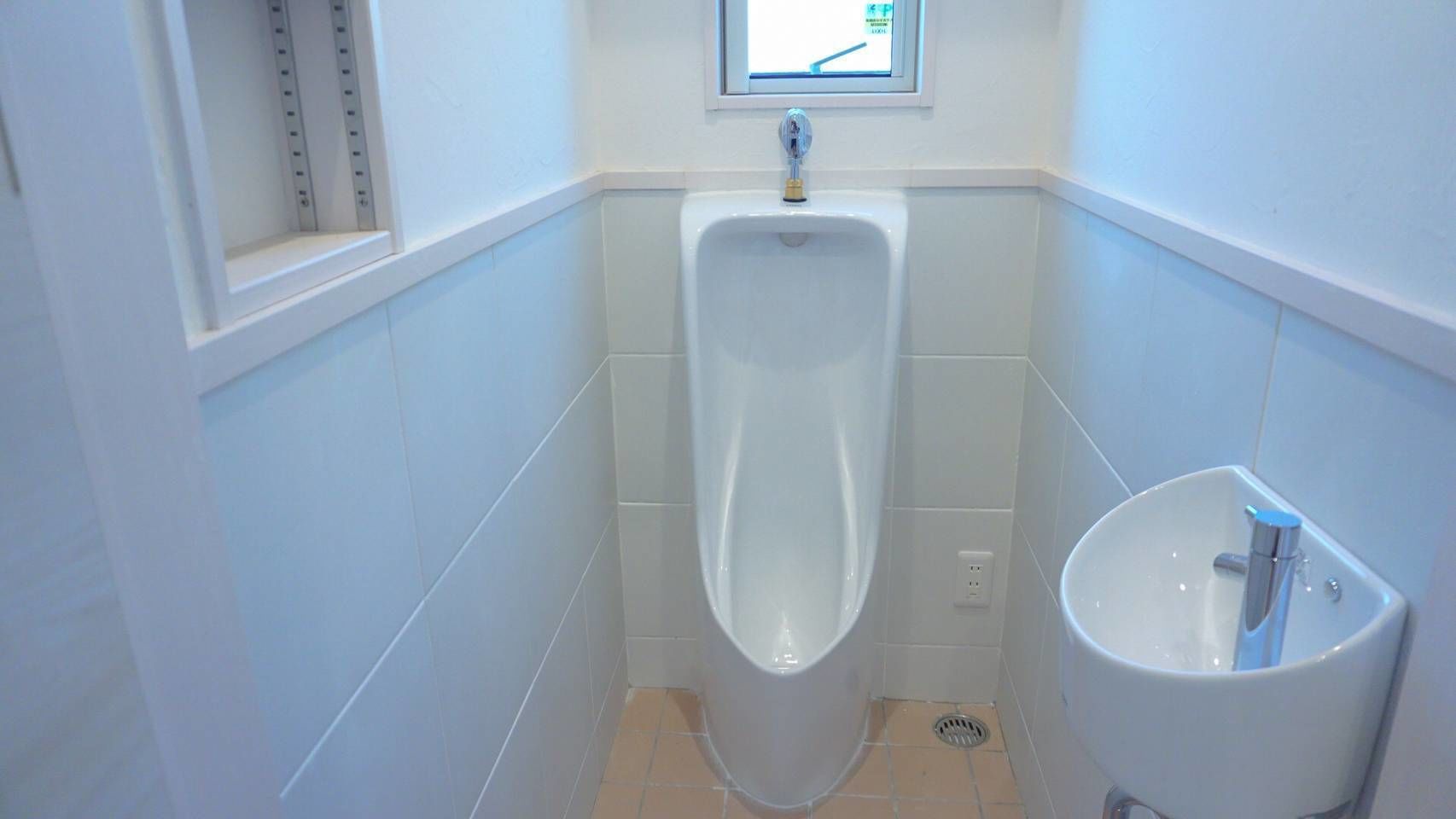 Baño de hombres con orinal, lavamanos y una ventana sobre el lavamanos.