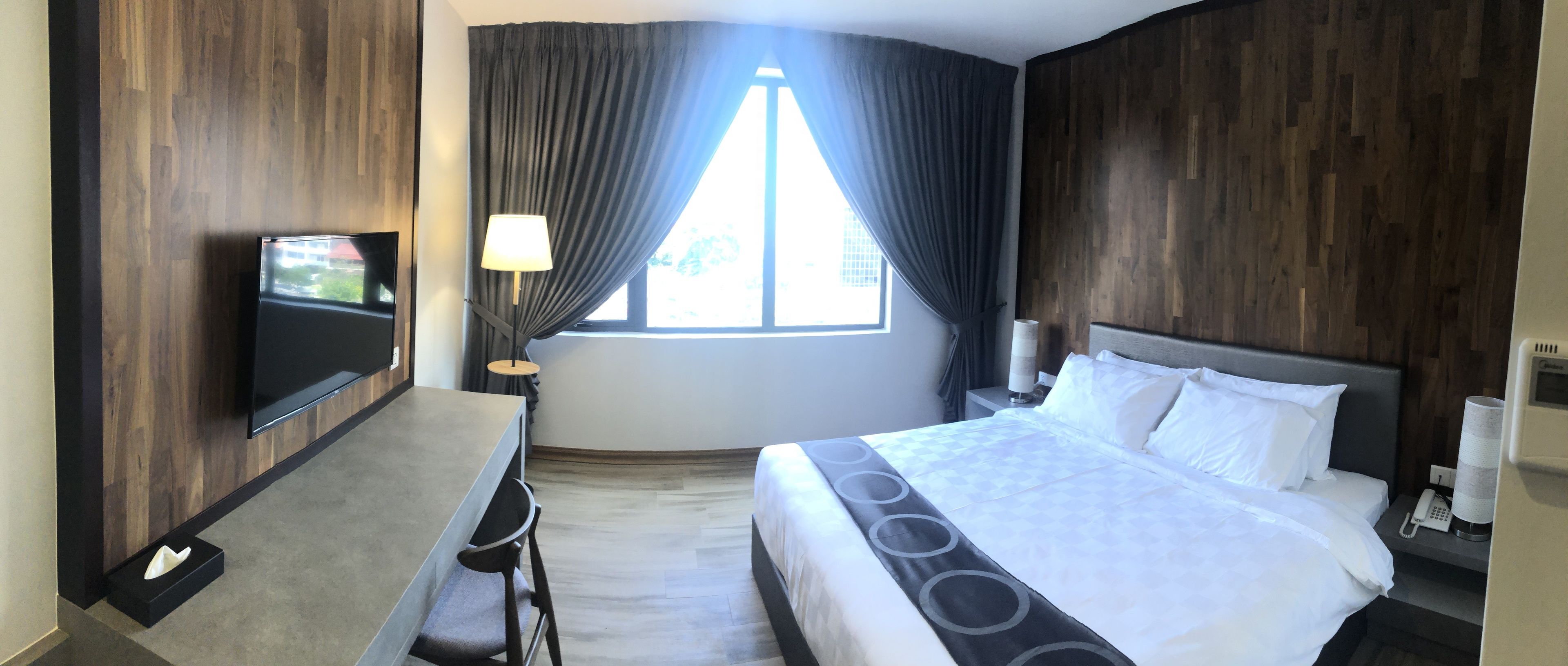 A hotel room with a bed, a desk, a TV, and a window with curtains.