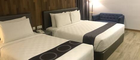 A hotel room with two beds, a bedside table with a phone, a lamp, and a blue chair.