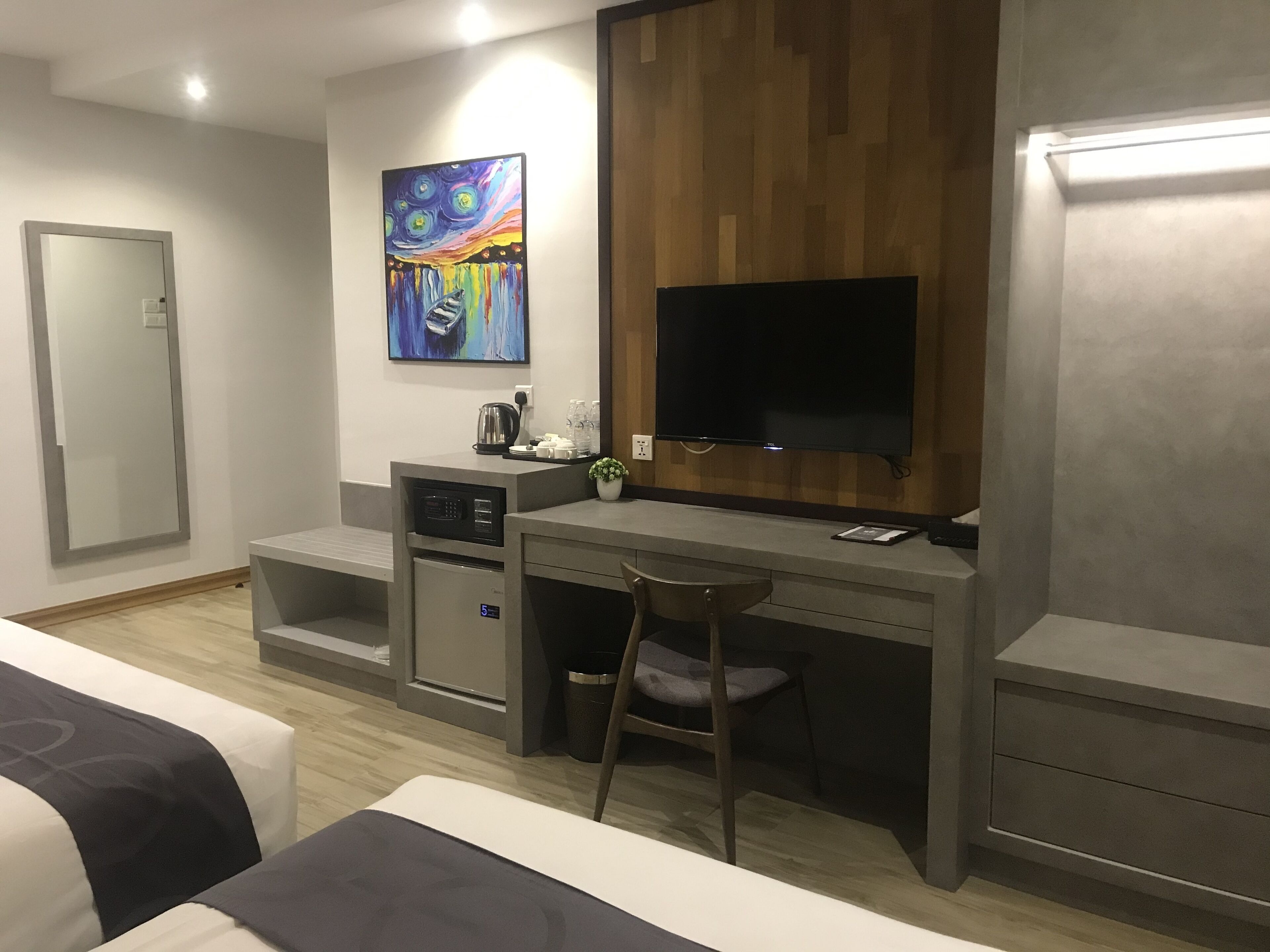 A modern hotel room with a kitchenette, a flat-screen TV, a painting, and a large mirror.