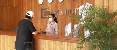 A reception desk at Frame Hotel with a wooden wall, multiple clocks, and a potted plant.