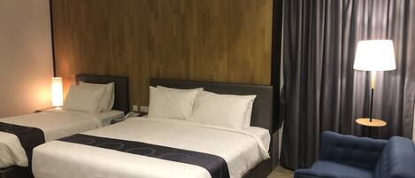 A hotel room with two beds, a blue armchair, a lamp, and a wooden headboard.