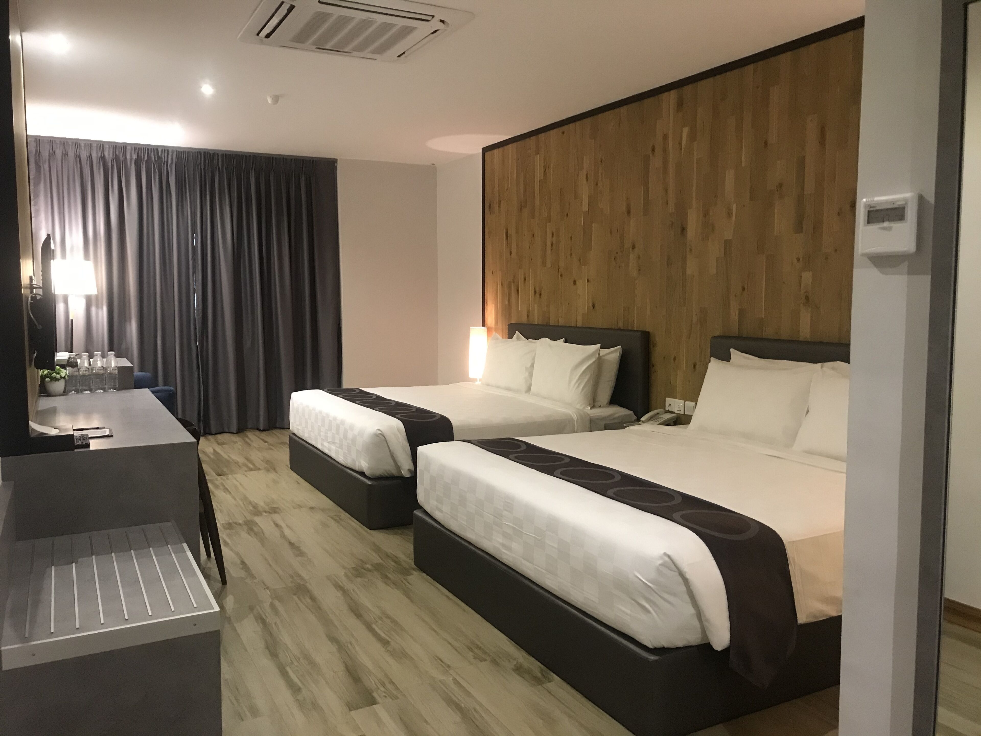 A hotel room with two beds, a desk with a chair, a mirror, and a wooden wall.