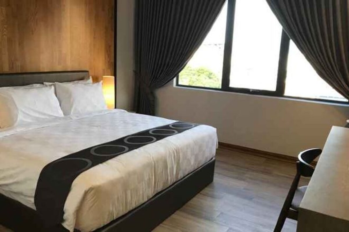 Una habitación de hotel con una cama grande, una mesita de noche y una ventana con cortinas.