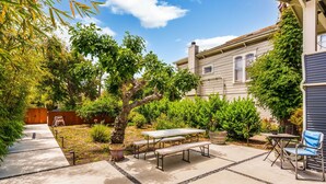 A patio area with a picnic table and chairs, surrounded by greenery and a house in the background. - Quiet, Comfortable & Clean. Easy Access to SF, Berkeley, Contra Costa (Oakland)