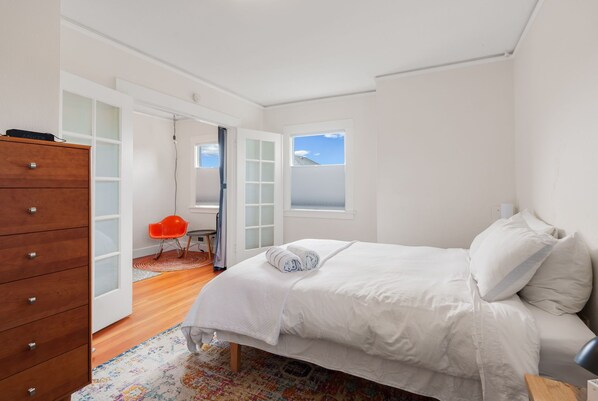 Une chambre à coucher avec un lit, une commode en bois, une chaise rouge et une fenêtre donnant sur un beau paysage.