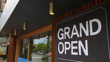 A sign that reads "GRAND OPEN" with a reflection of a street scene in the window.