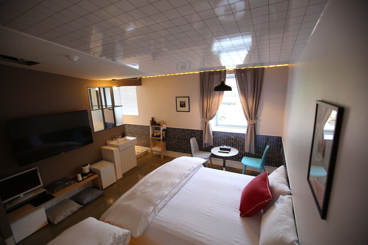 Habitación de hotel con una cama grande, televisión, escritorio con computadora, baño pequeño y ventana con cortinas.