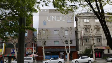 A hotel named ONDO with a modern facade, a sign indicating a grand opening, and several parked cars on the street.