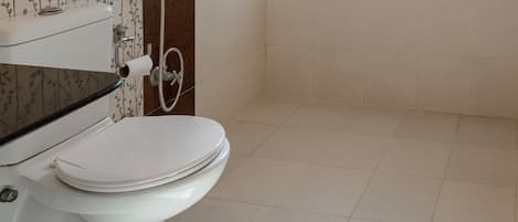 A bathroom with a toilet, a shower, and a window with blinds.