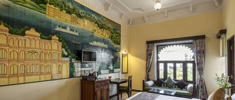 A hotel room with a large mural, a bed, a desk, and a window with a view.