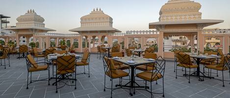 A rooftop restaurant with outdoor seating, featuring tables and chairs arranged under ornate, multi-tiered structures.