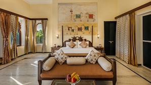 A spacious hotel room with a large bed, a sofa, and a glass coffee table with fruit.