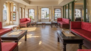 A spacious room with red sofas, wooden tables, and large windows offering a city view.