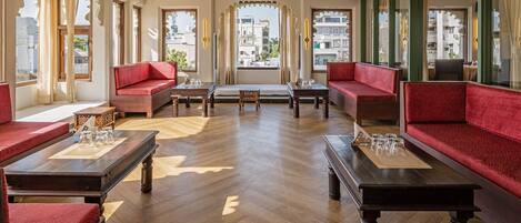 A spacious room with red sofas, wooden tables, and large windows offering a city view.