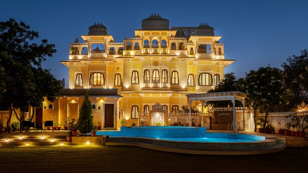 A large, illuminated building with multiple balconies and a swimming pool in the foreground.