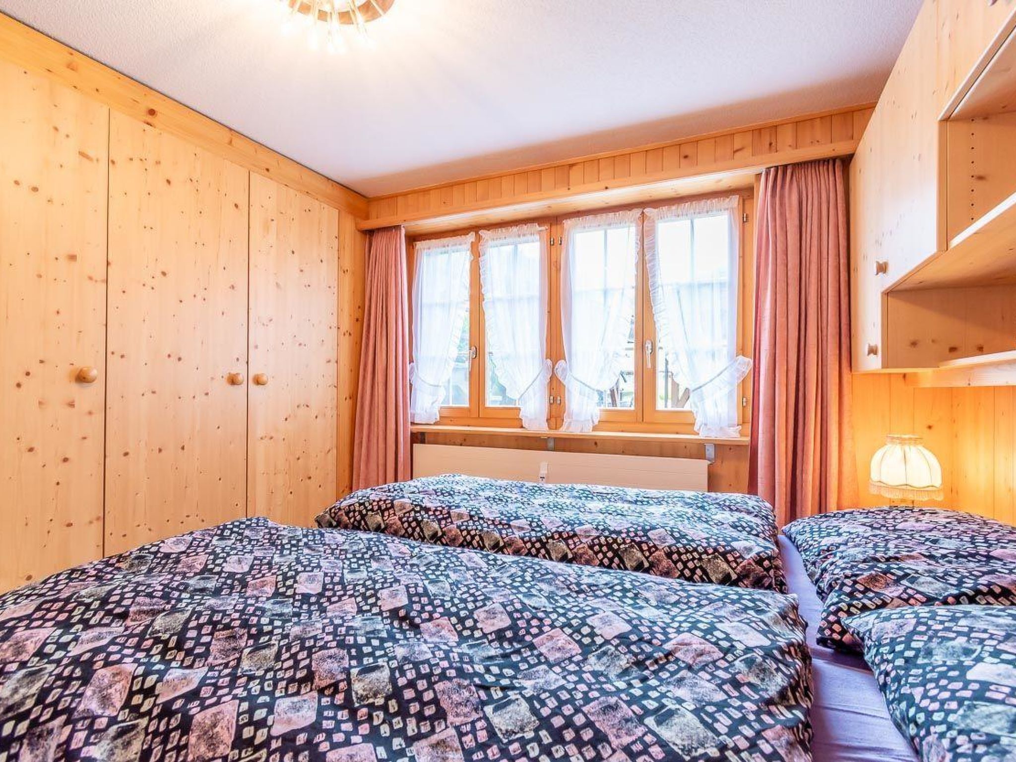 A room with wooden walls, a window with curtains, and two beds with patterned bedding.