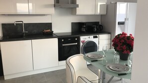Eine moderne Küche mit weißen Schränken, einer schwarzen Arbeitsplatte, einem Geschirrspüler, einer Kaffeemaschine und einem Kühlschrank.