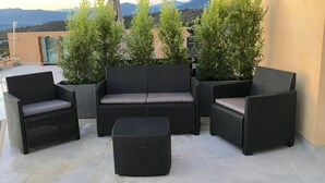 Eine Terrasse mit Korbmöbeln, darunter eine Sitzecke und Stühle, umgeben von Topfpflanzen.