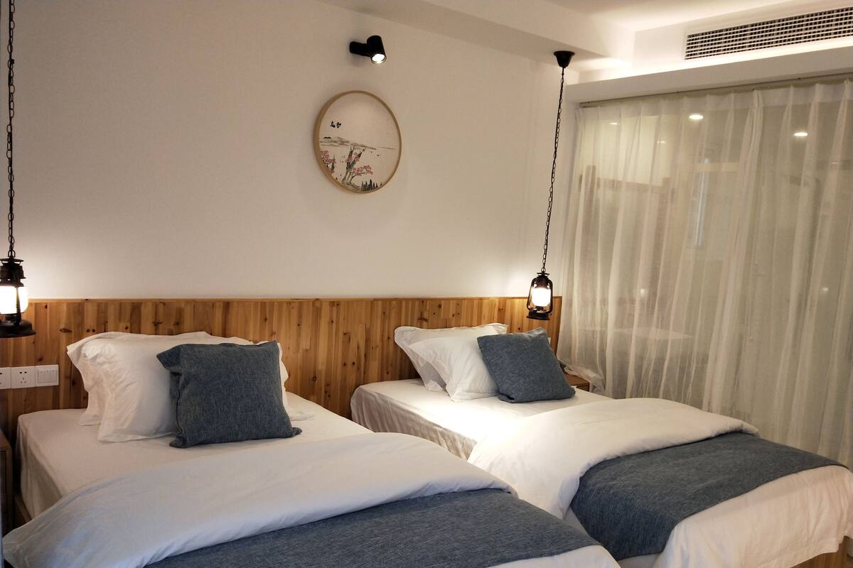 Habitación de hotel con dos camas, cabeceros de madera, ropa de cama blanca y un reloj fijado a la pared.