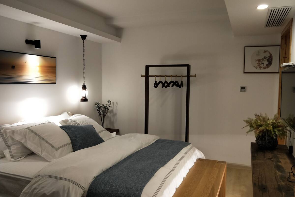 Un dormitorio moderno con una cama grande, un banco de madera, una lámpara fijada a la pared y un perchero.