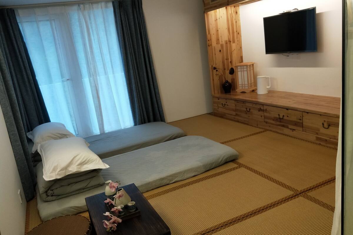 Habitación de hotel con cama, televisor montado en la pared, mueble de madera y suelo de tatami.