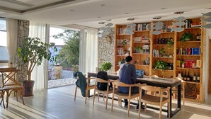 A spacious room with a large wooden bookshelf filled with books and decorative items, a dining area with wooden chairs, and a large window providing natural light. - 25 Degree Sea Boutique Homestay (Zhoushan)