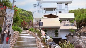 A modern two-story hotel with a stone facade, a staircase leading to the entrance, and a sign indicating a 25th anniversary. - 25 Degree Sea Boutique Homestay (Zhoushan)