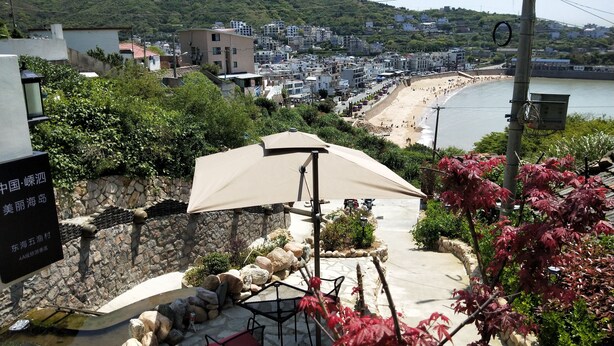 A coastal town with a beach, stone walls, and a patio area with a table and chairs. - 25 Degree Sea Boutique Homestay (Zhoushan)
