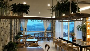 A restaurant with wooden tables and chairs, large windows with curtains, and potted plants. - 25 Degree Sea Boutique Homestay (Zhoushan)