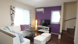 Ein Wohnzimmer mit Sofa, Hocker, Couchtisch, Flachbildfernseher und einer Treppe.