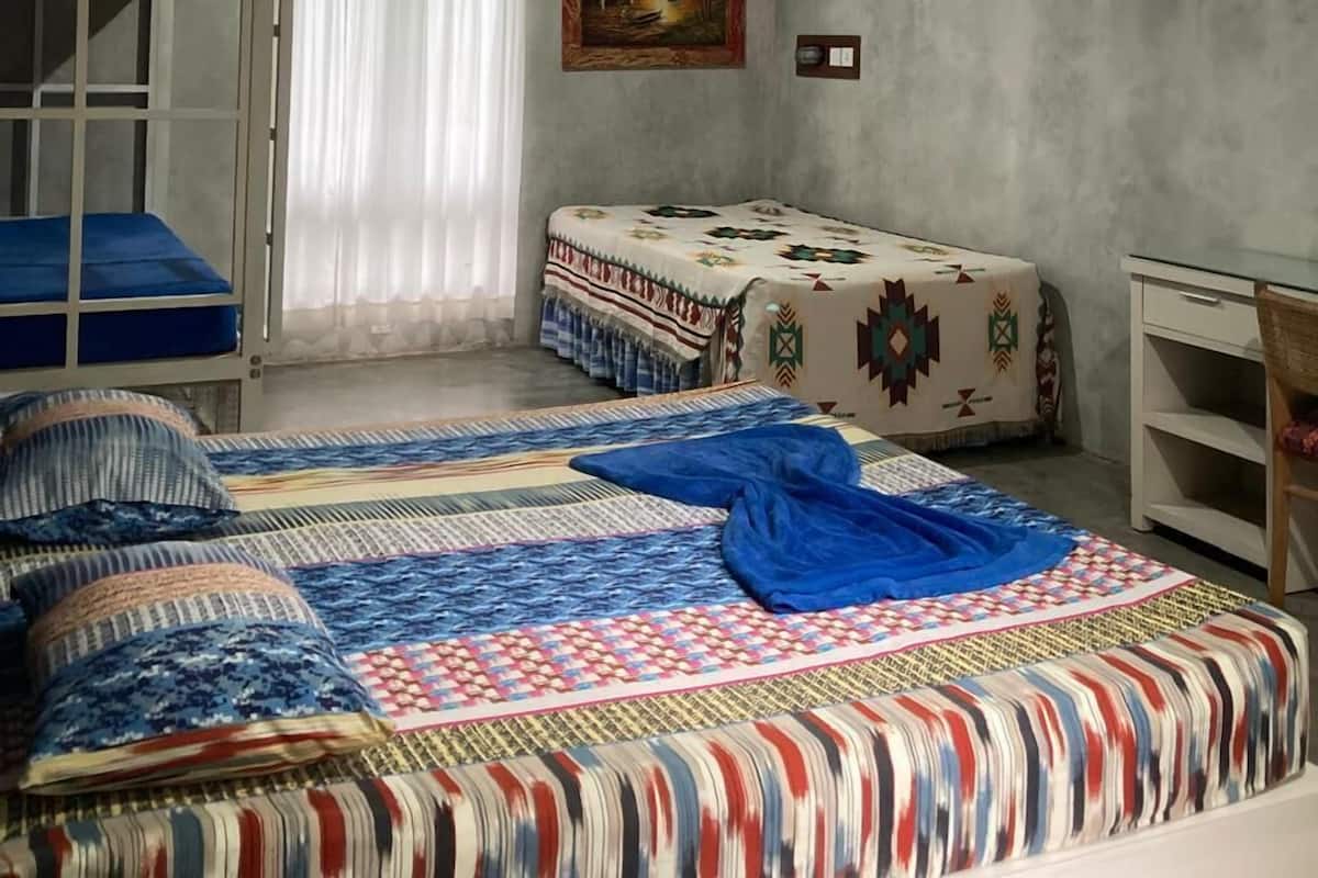 Ein Schlafsaalzimmer mit Etagenbetten, einem Schreibtisch, einem Stuhl, einem Bett mit gemusterten Bettwaren, einem Bild an der Wand und einem Fenster mit Vorhängen.