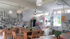 A restaurant with wooden tables and chairs, hanging lights, and a mural on the wall. - Bali Bobo Hostel (Jimbaran)