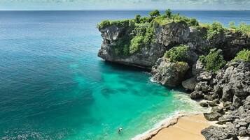 A coastal landscape with a rocky cliff, clear turquoise waters, and a sandy beach.