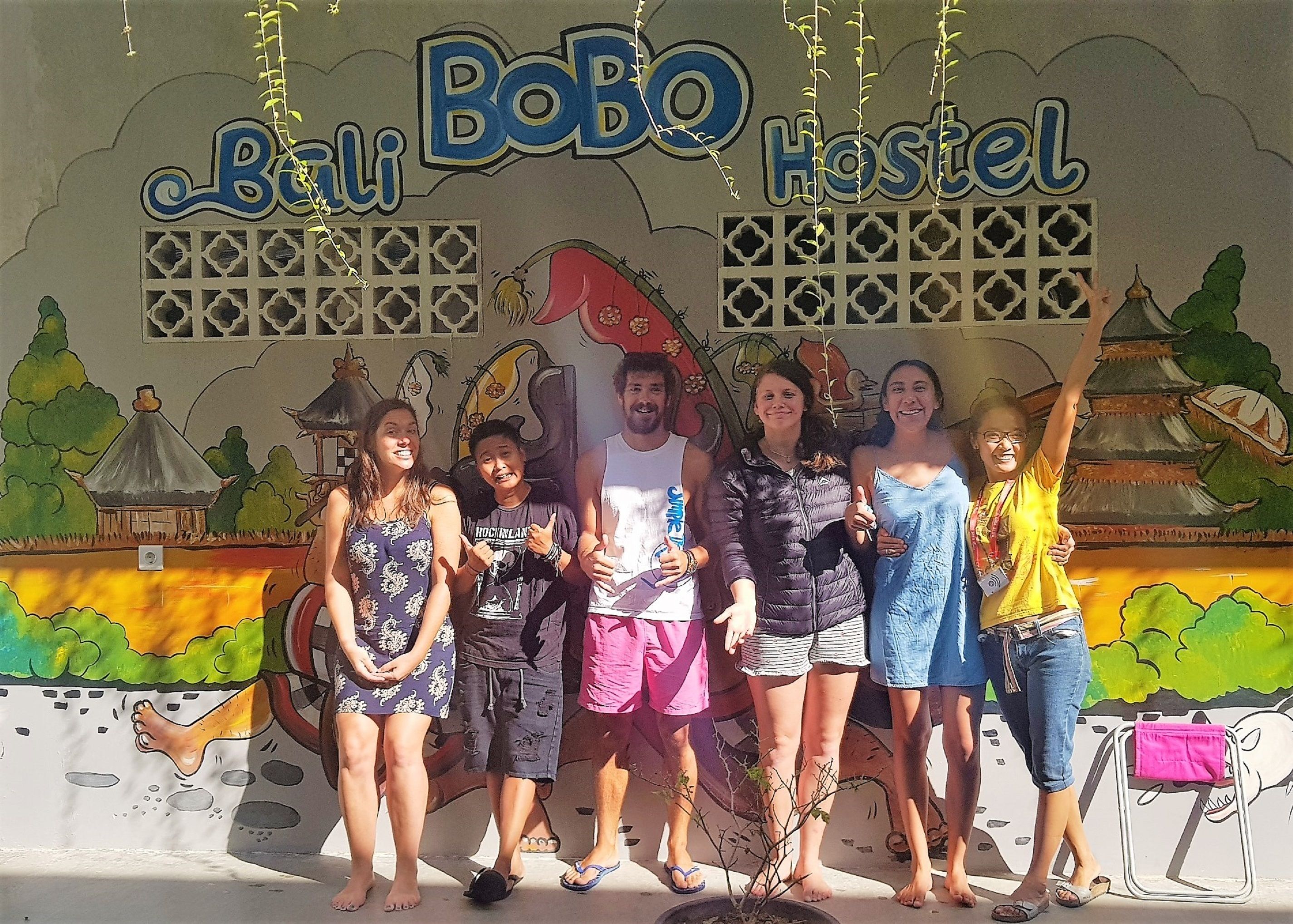 Un groupe de personnes posant devant un mur sur lequel on peut lire : « Bali Bobo Hostel ».